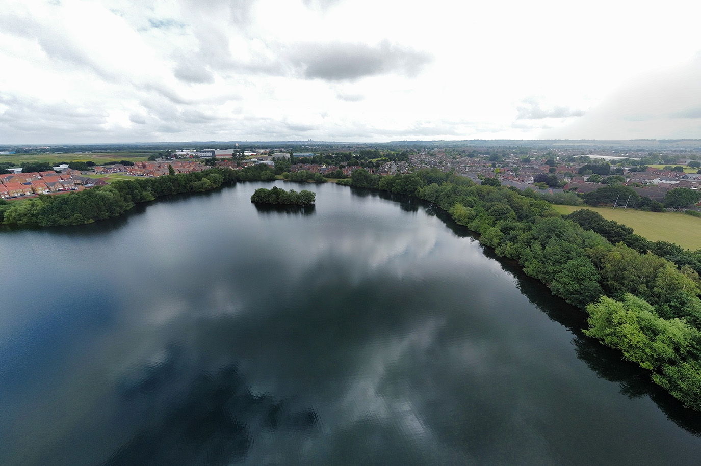Drone photography shot of North Hykeham, displaying a large lake, trees and a village.