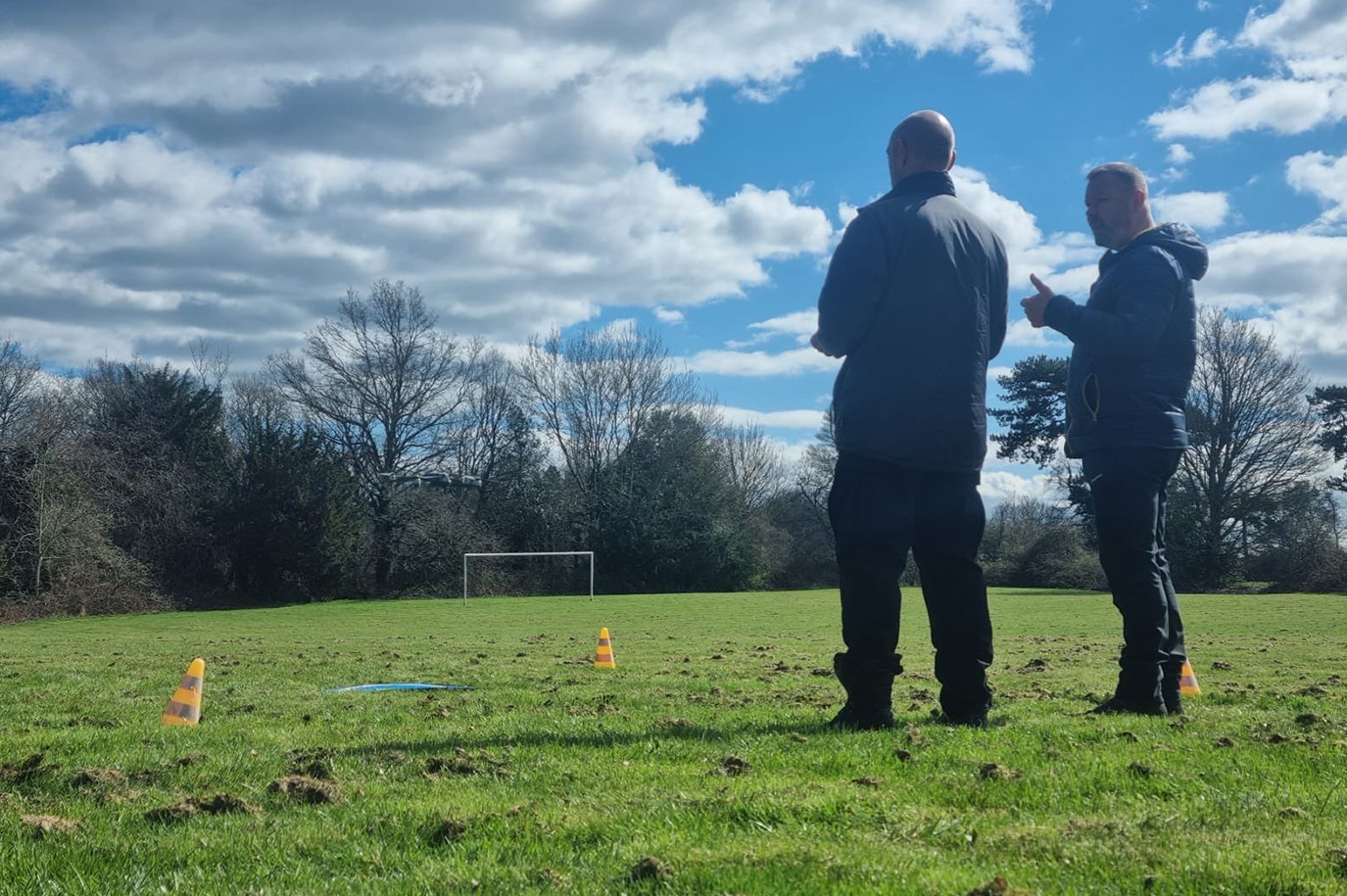 Two men stood outside looking at a drone landing pad. One man is speaking to the other.