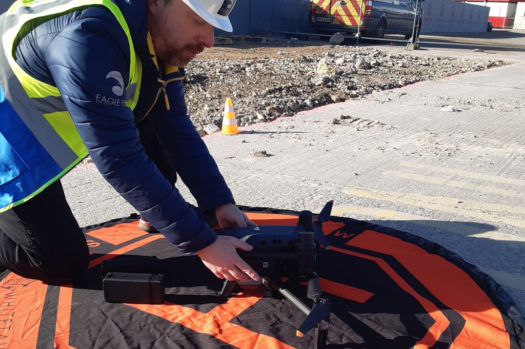 Man holding drone on landing pad preparing to inspect construction site.
