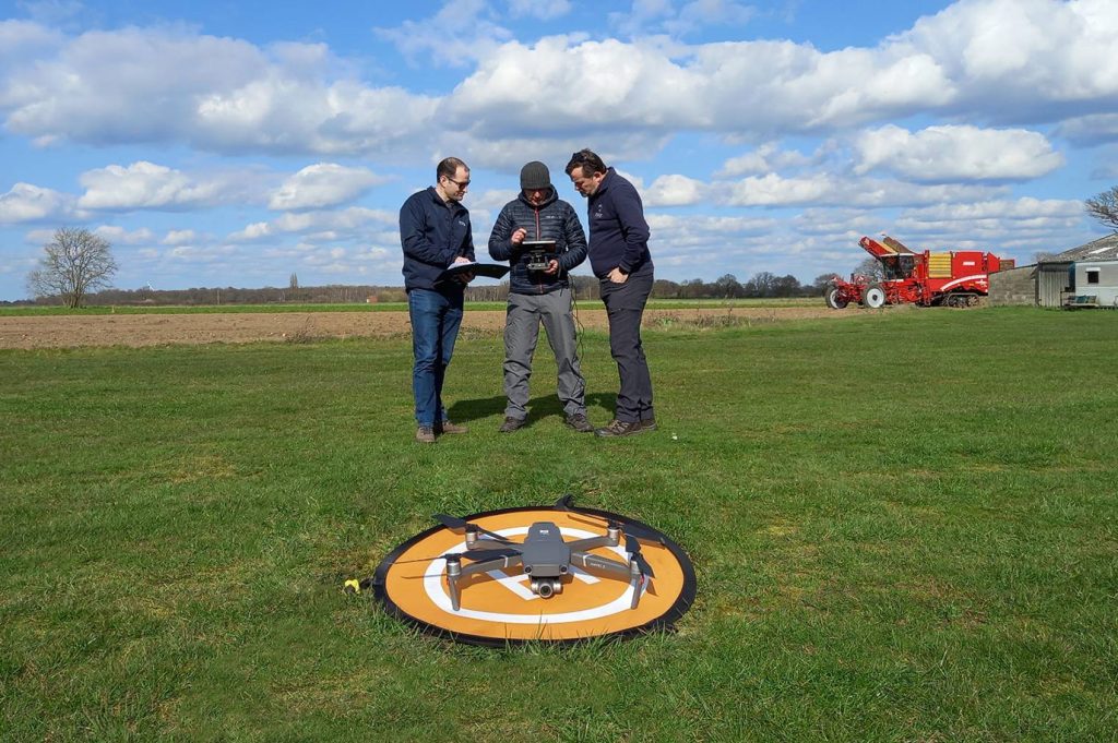 Image of drone on a landing pad on the floor in front of three men.